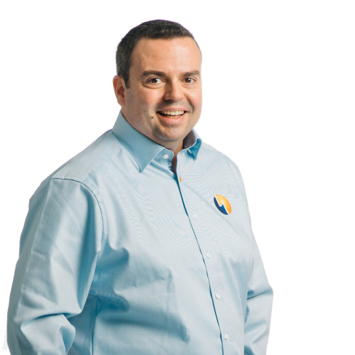 Ein Mann in einem hellblauen Hemd mit einem Logo auf der Brust lächelt freundlich.