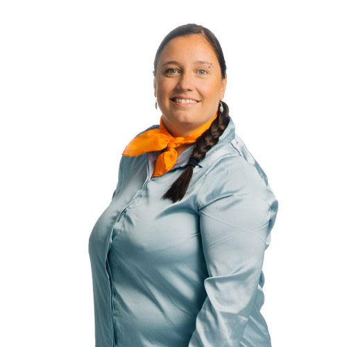 Eine Person mit geflochtenen Haaren, einem orangefarbenen Halstuch und einem hellblauen Oberteil steht lächelnd seitlich.