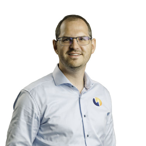 Ein Mann mit Brille und lächelndem Gesicht trägt ein hellblaues Hemd mit einem Logo auf der Brust.