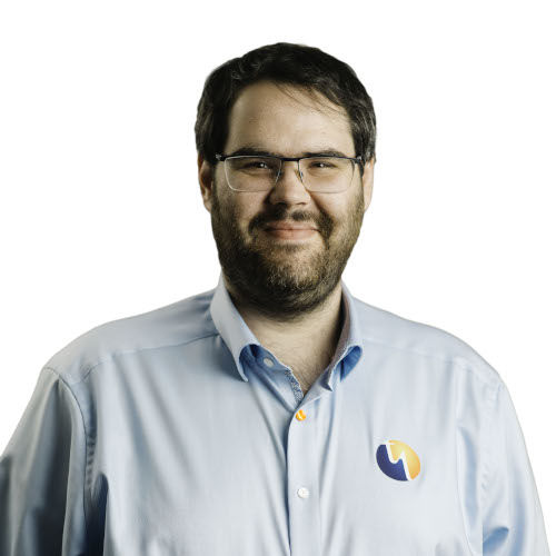 Ein Mann mit Brille und Bart trägt ein hellblaues Hemd mit einem Logo auf der Brust.