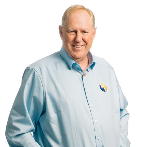 Ein Mann mit blondem Haar und Lächeln trägt ein hellblaues Hemd mit einem Logo auf der Brust.